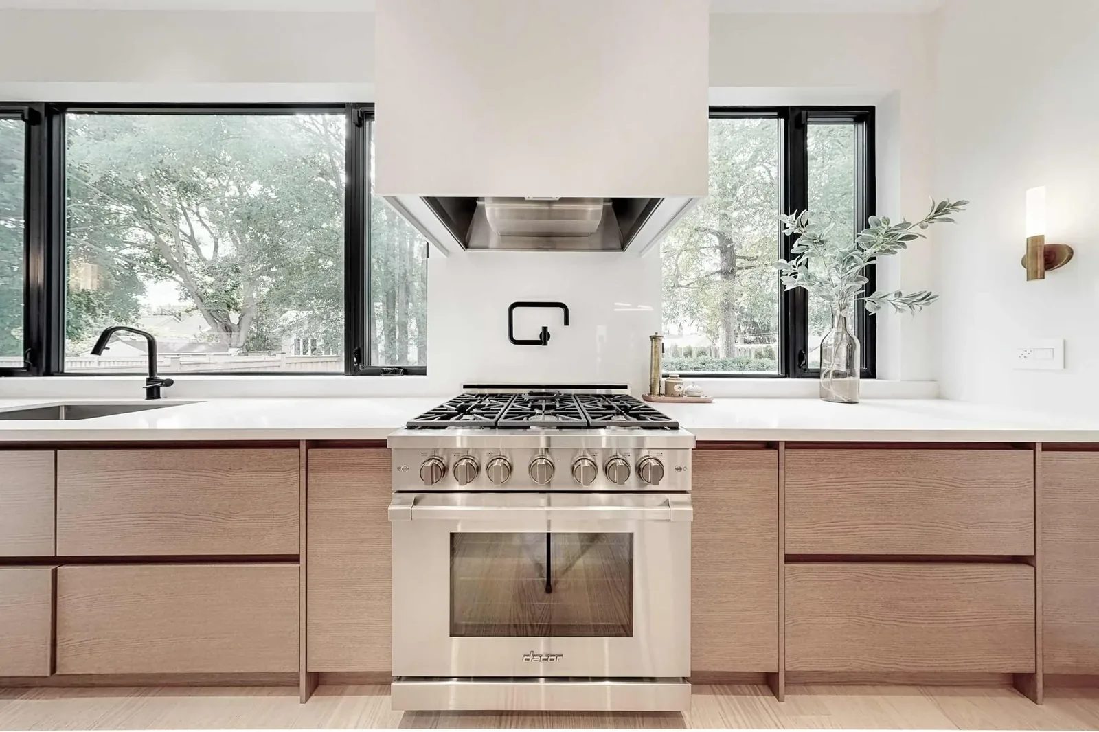 Gas cooktop in the foreground looks across an open-concept living room with a linear fireplace, wall TV, and cognac lounge chairs.