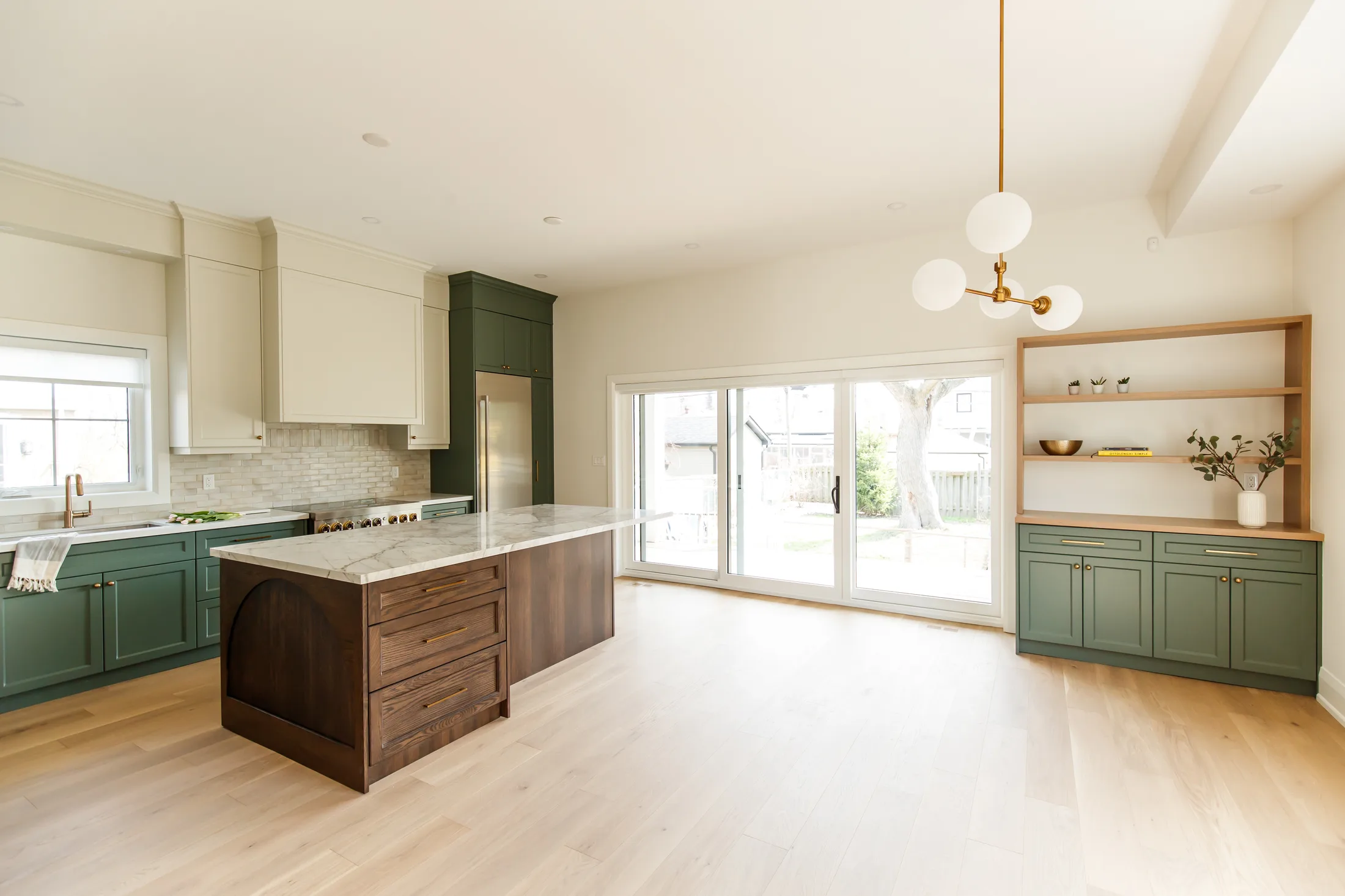 Open concept kitchen and dining room with an arched oak island, green cabinetry, and a wall of sliding patio doors.