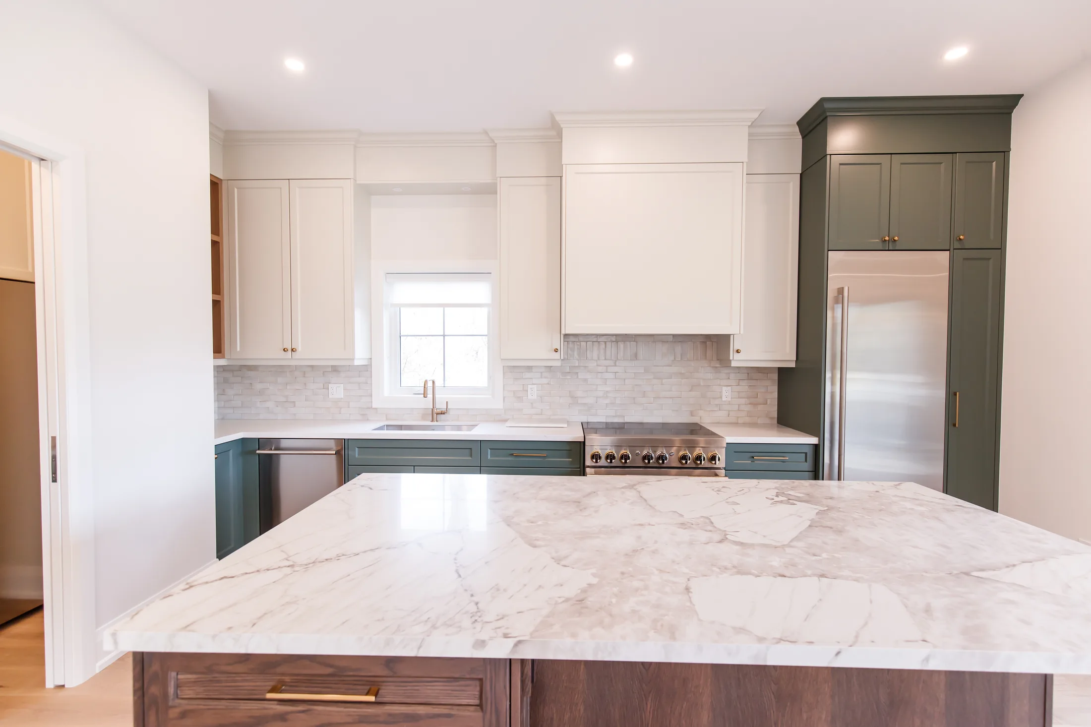 Chef kitchen with cream cabinets, green fridge tower, pro gas range and a book-matched marble island.