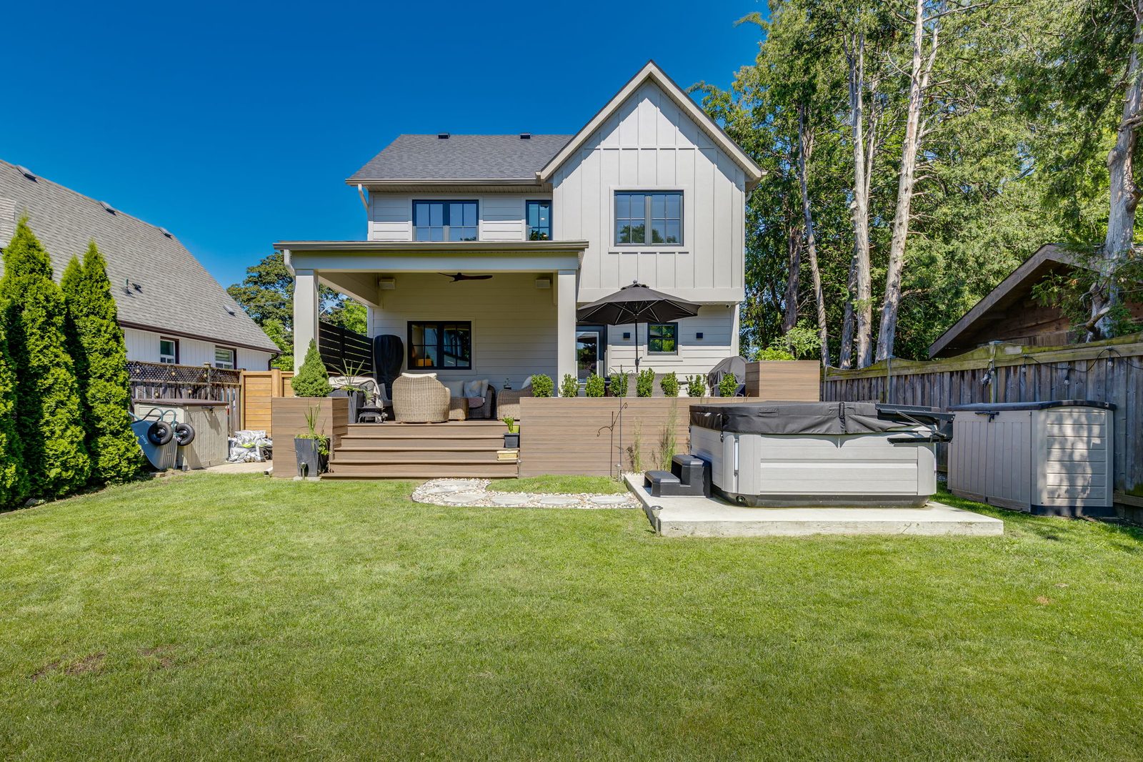 Rear elevation of the finished two-storey home with board-and-batten siding, a covered porch, a raised composite deck and a wide lawn.